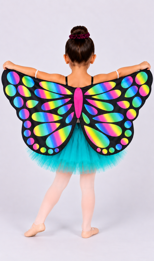 A young girl from behind wearing a black butterfly wing costume with a vibrant rainbow gradient pattern and a turquoise tutu skirt, posing against a light gray studio background.